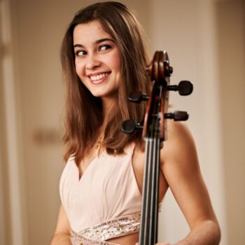 Annabel Hauk blickt lächelnd in die Kamera. An ihre Schulter gelehnt sieht man die Schnecke ihres Violincellos.