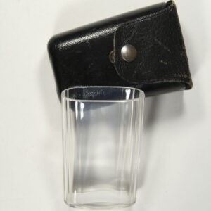 man sieht die Fotografie eines Glases und eines kleinen Mäppchens aus schwarzem Leder, das schräg dahinter liegt.